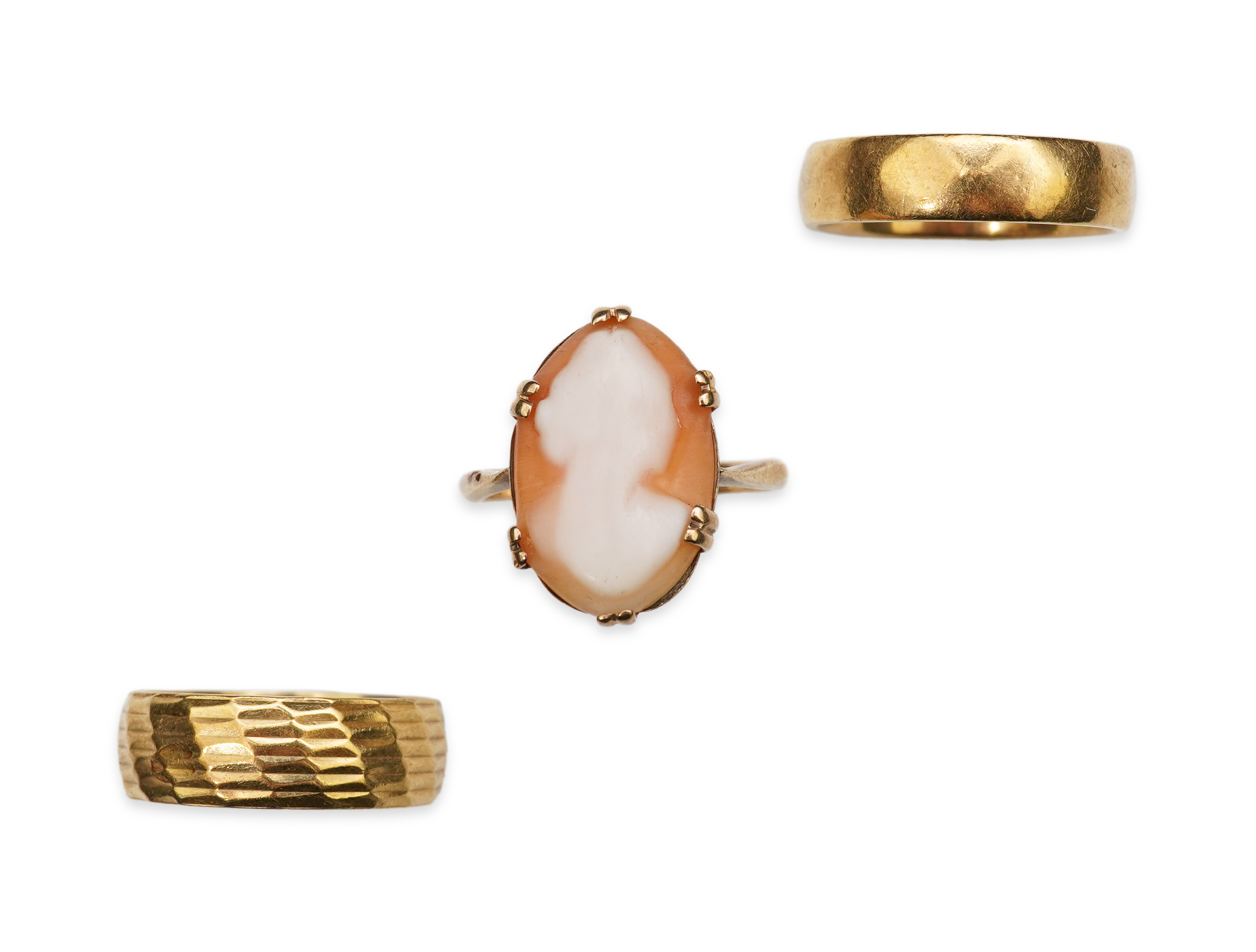 Three rings, comprising: two 18ct gold wedding bands, of planished and textured design, sizes K and L respectively, each with British hallmarks, combined gross weight approximately 11 grams; and a shell cameo ring mounte